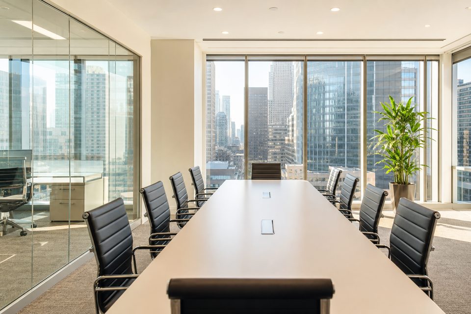 Tidy office meeting room with a white table and black chairs beside city windows